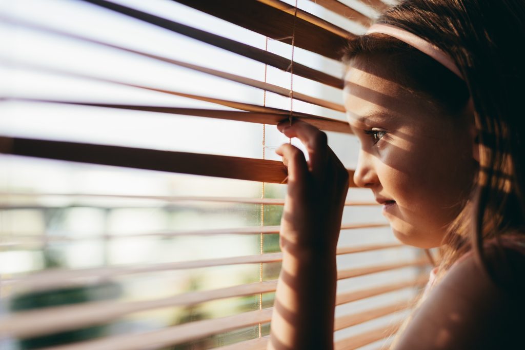 Young girl looking through blinds